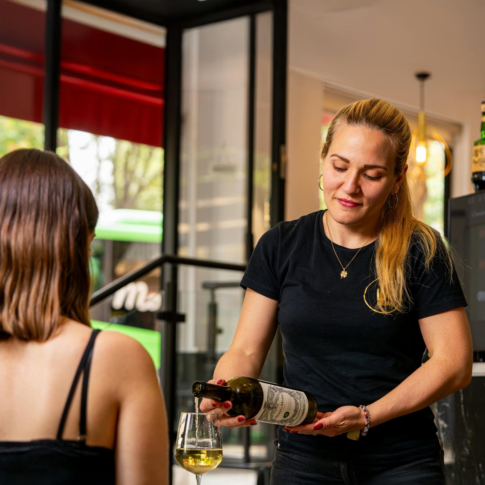 A waitress pours wine for a customer in a cozy restaurant setting.